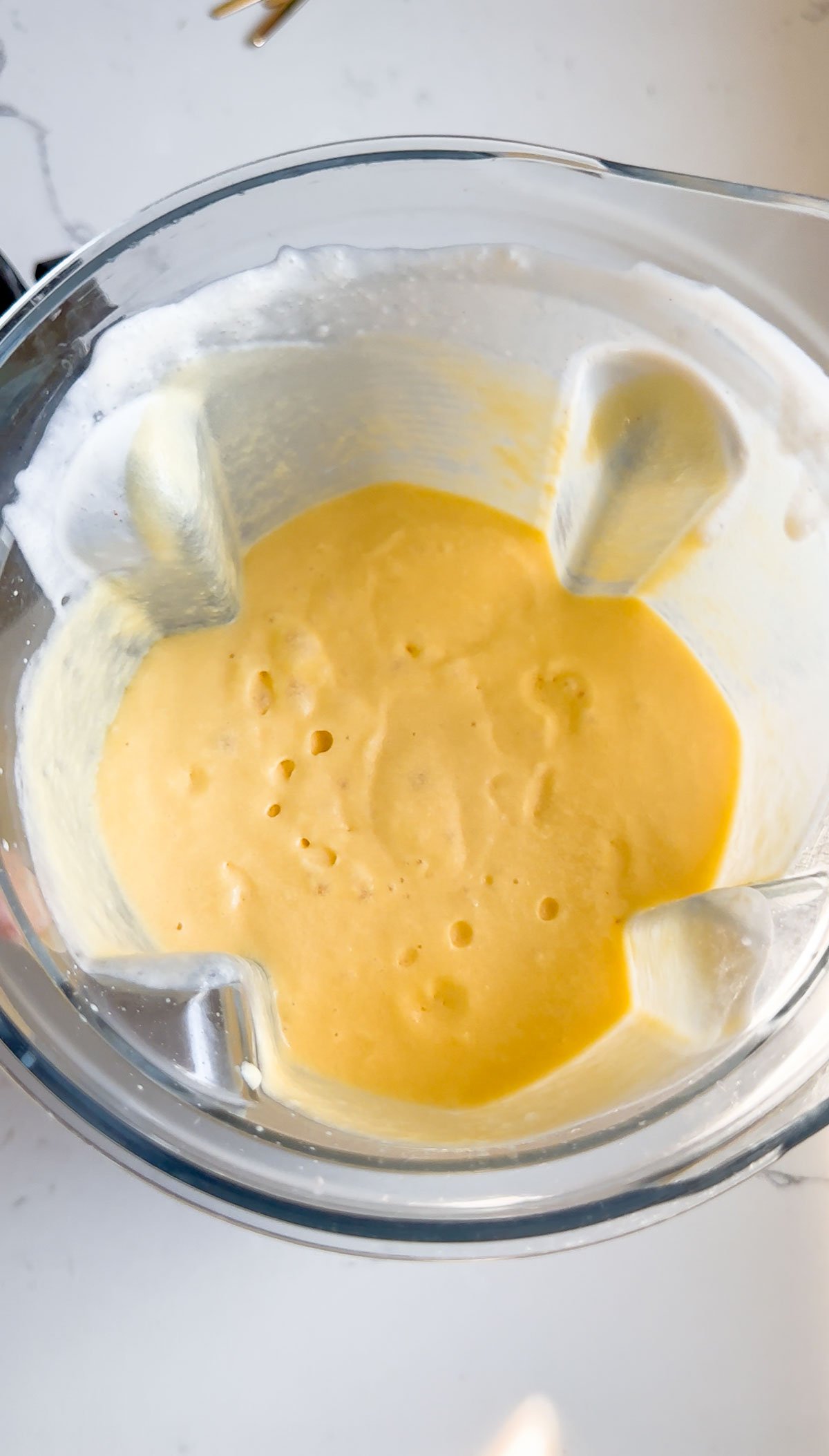 liquid peach ice cream mixture in blender on marble surface