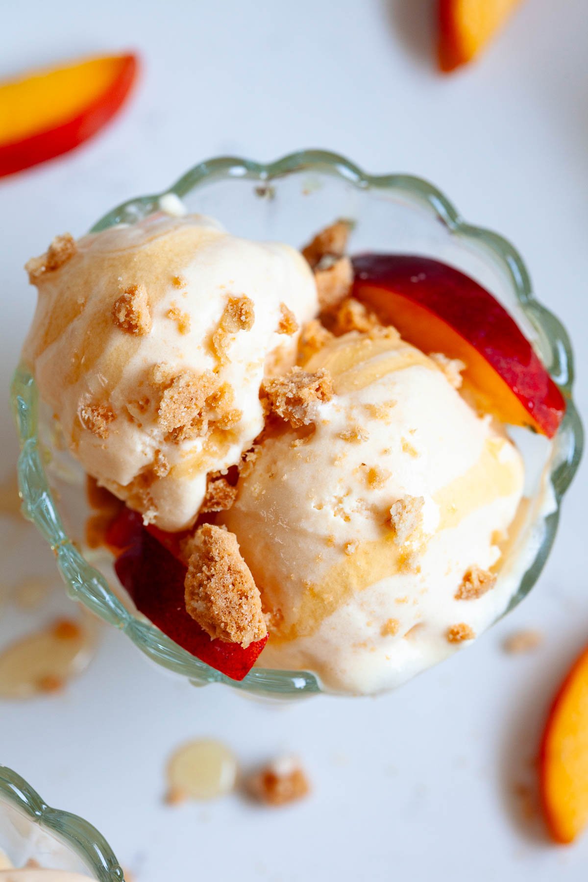 close up of peach kefir ice cream in glass bowl with drizzled honey, peach slices, and cookie crumbles
