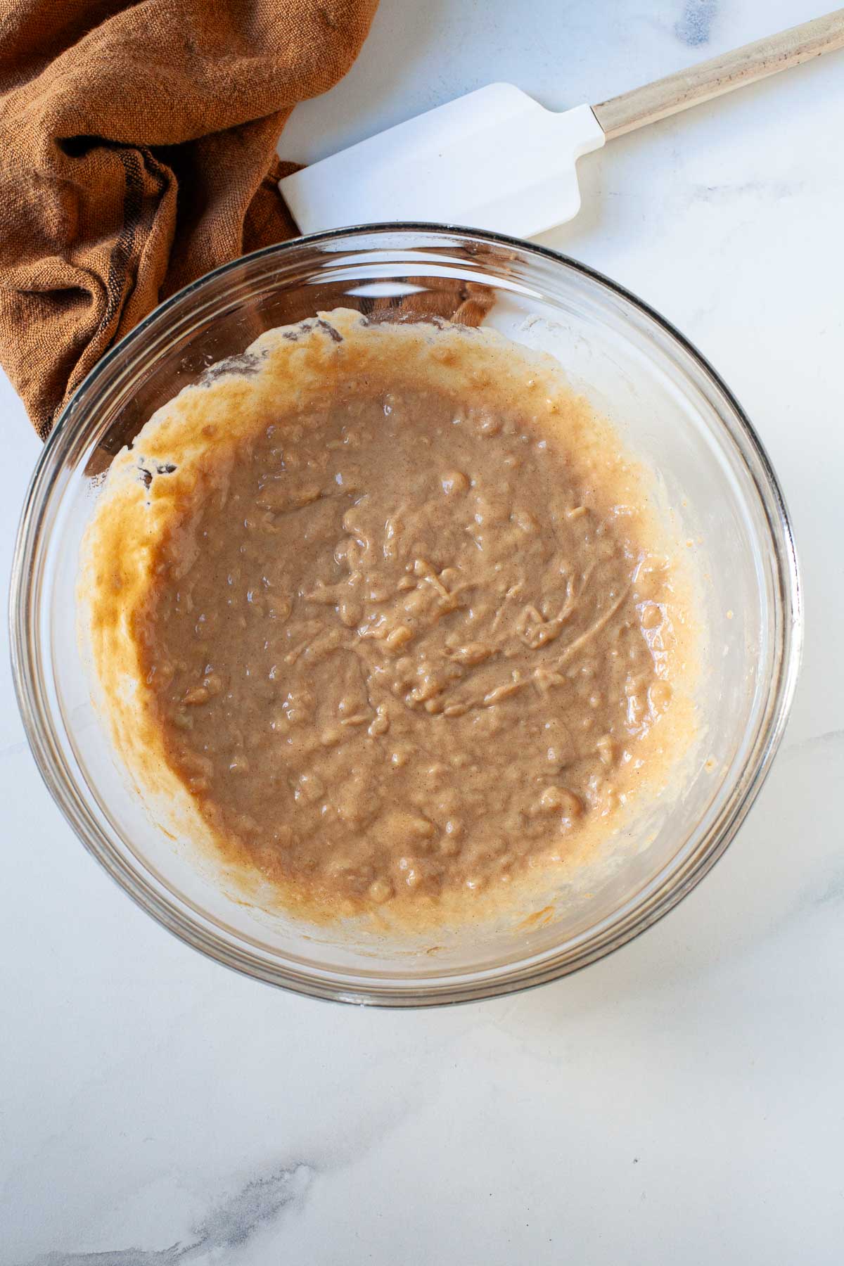 mashed banana, peanut butter and syrup mixed together in glass bowl with burnt orange dish cloth