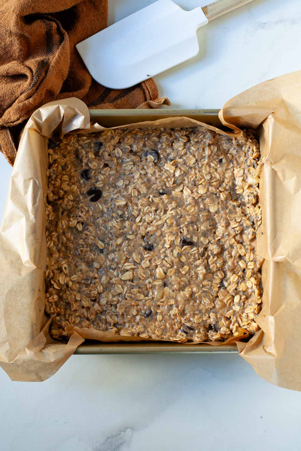 mixture for peanut butter banana oat bars with chocolate chips in a parchment paper lined square pan