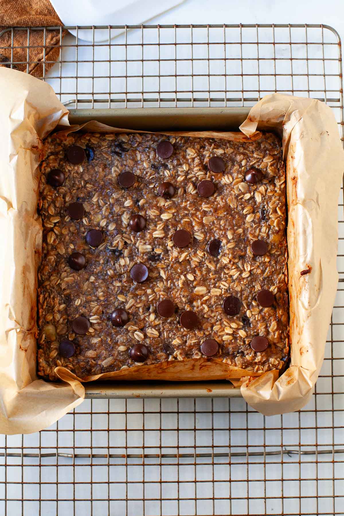 baked peanut butter banana oat bars in parchment paper lined square pan on wire rack