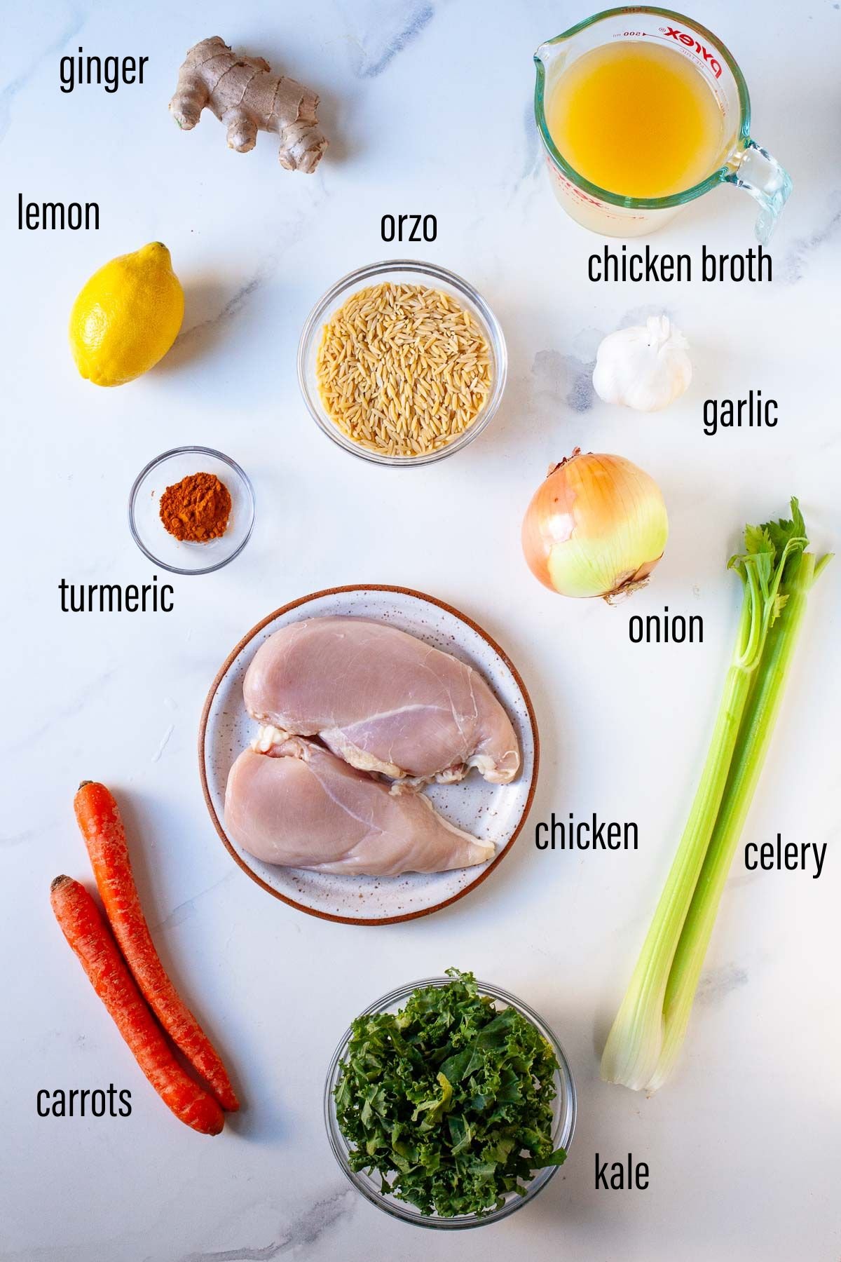 ingredients for chicken orzo soup with turmeric and ginger with text overlay on white marble surface
