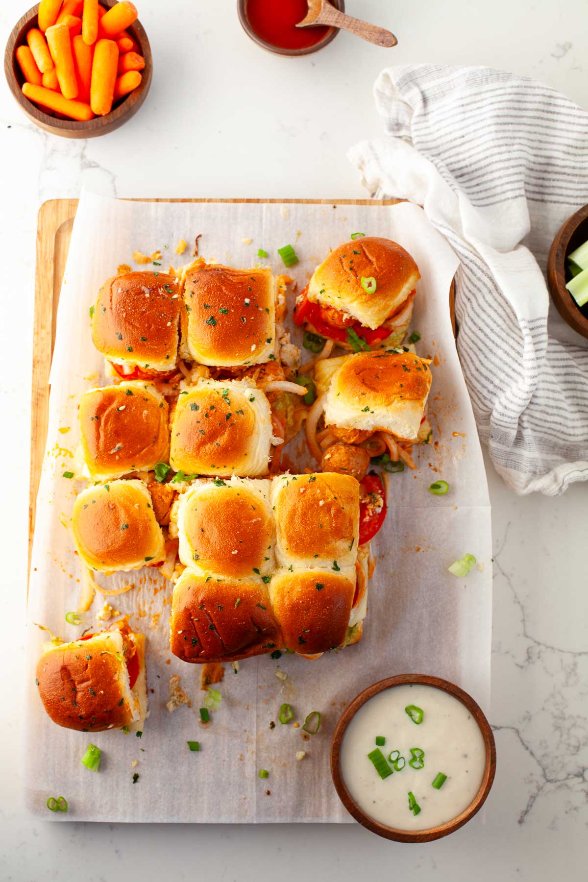 buffalo chicken meatball sliders pulled apart on parchment paper with carrots, celery sticks and blue cheese dressing