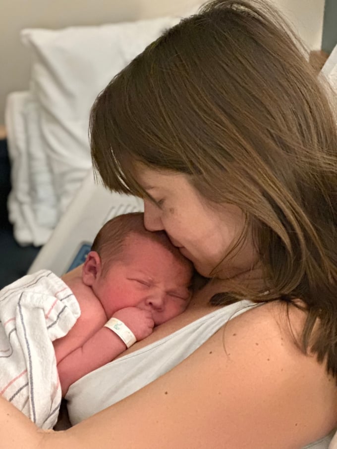 woman in hopsital bed with baby laying on her chest wrapped in a blanket